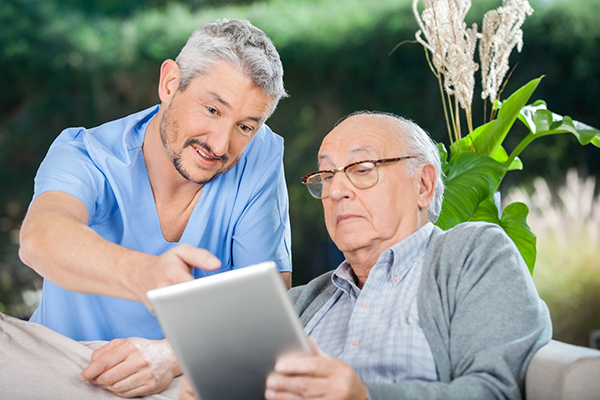 Male nurse showing something to senior man on digital tablet at nursing home porch